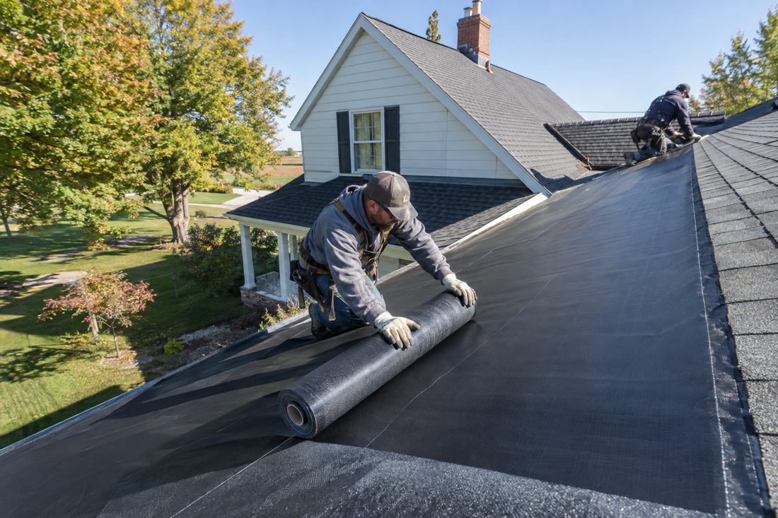 New ice and water shield being rolled out along a valley at a two-story Iowa farmhouse-style home with maples in Waterloo, IA